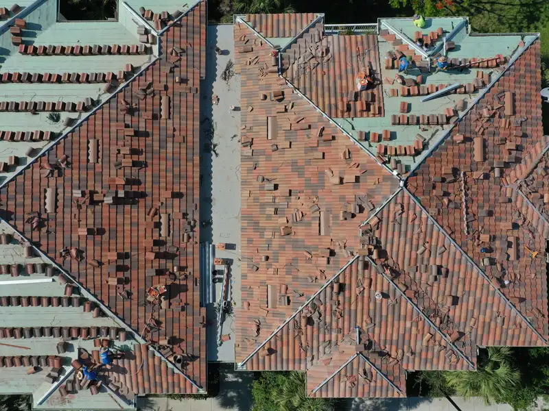 Top-down drone view of crews laying new tile across a large roof